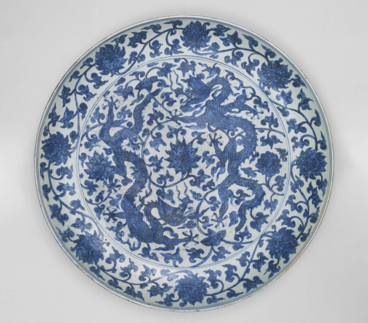 Grande assiette en <br />
porcelaine bleu et blanc <br />
avec des motifs du dragon <br />
parmi des lotus imbriqués